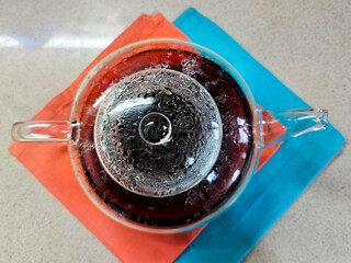 Glass transparent teapot with hot tea on colored napkin on a table top. Drops of condensate on inner surface. Tea ceremony. View from above. Selective focus