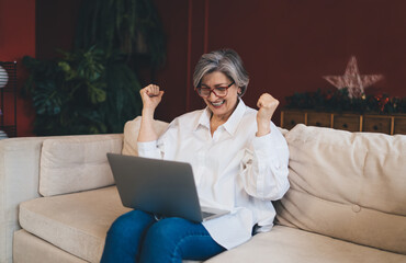 Cheerful pensioner woman celebrating victory with laptop