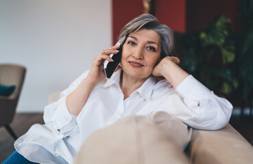 Smiling mature woman talking on smartphone on sofa