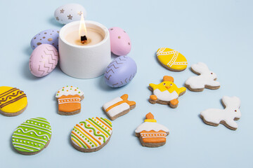 Easter gingerbread with icing, Easter eggs and candle on blue background
