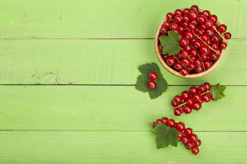 Red currant berries in a wooden bowl with leaf on the green wooden background. Top view with copy space for your text