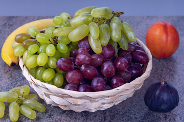 berries of white and red grapes and fresh fruits in a straw basket on a dark wooden background - 587075596