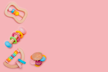 Cute set of wooden rattles for baby on pink background. Eco-friendly toys for newborns in the colors of the rainbow. Flat lay, copy space.