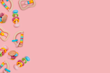 Many cute wooden rattles for baby on pink background. Eco-friendly toys for newborns in the colors of the rainbow. Flat lay, copy space.