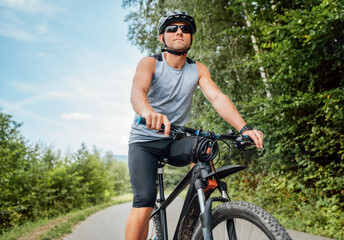 Obraz premium Portrait of happy man dressed in cycling clothes, helmet and sunglasses riding a bicycle on the out-of-town bicycle path. Active sporty people concept image.