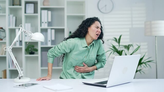 Sick young woman suffering from stomach ache during computer work holding belly feeling gastritis or abdomen colon pain at office workplace indoors worker employee Digestion poisoning problem indoor