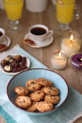 Plate of chocolate pralines, bowl of cookies, cups of tea, glasses of juice and lit candles on the table. Selective focus.