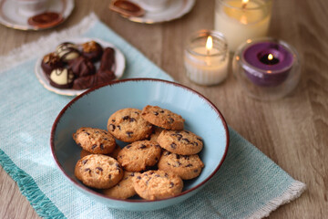 Plate of chocolate pralines, bowl of cookies, cups of tea, glasses of juice and lit candles on the table. Selective focus.