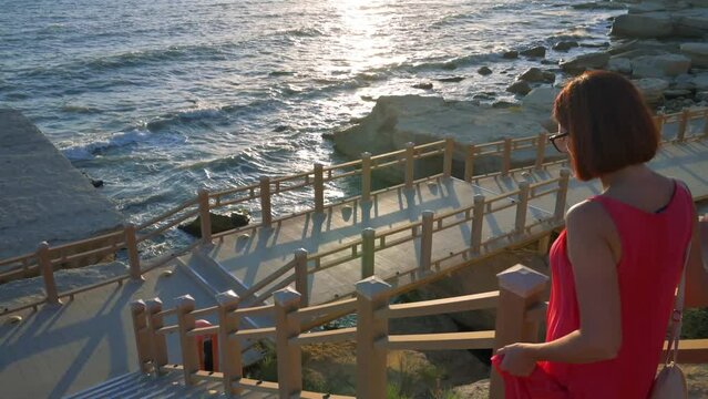 Woman in red dress walking down tairs to the Baltic sea. Woman impressed with the nature. 4k footage UHD 3840x2160 