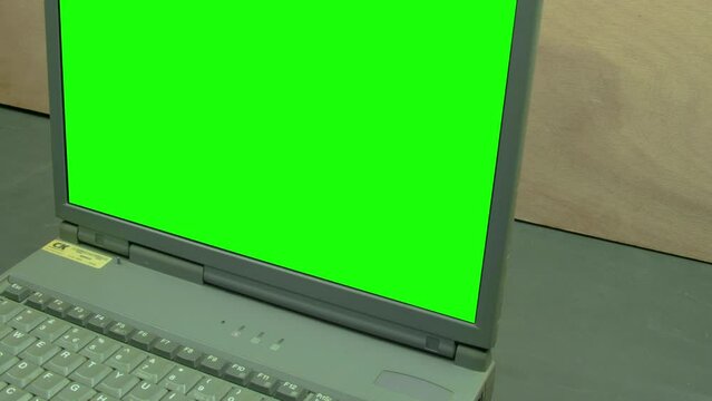 Computer laptop keyboard green screen ready for keying. Camera dolly mouse vintage IT old technology.. Camera moving dolly. 90's workspace computer laptop on a black table, wood grain vintage