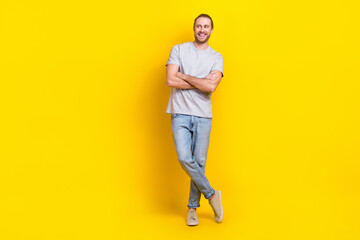 Fototapeta na wymiar Full size photo of optimistic handsome man gray t-shirt denim pants arms folded look empty space isolated on yellow color background