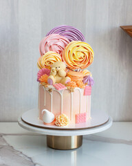 Pastel pink birthday cake decorated with cute chocolate teddy bear, meringue swirls and candy on grey background