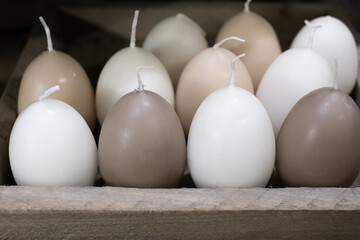 Beautiful candles in light pastel colors as Easter eggs on a wooden shelf in the background