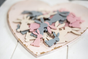 Beautiful playful white, pink and gray wooden Easter bunny figurines on an antique white wooden heart shaped tray on a white wooden table.