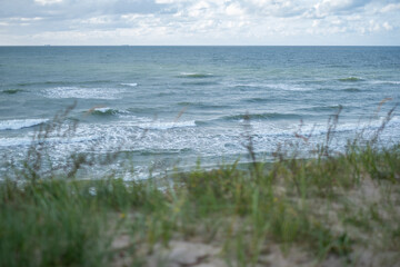 The wind sways the sea and the green grass in the sand dunes. Waves in the sea in windy weather in the background. Copyspace