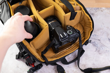 Man packing camera lens to his bag. Camera Photography Design Studio Lens Concept. Camera and backpack stands on a wooden table.