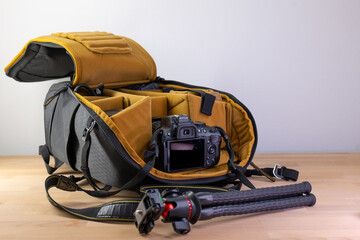Stylish Camera Bag with Accessories on Wooden Table. Professional Camera Equipment. Сamera bag with a mustard yellow interior is displayed open on a wooden table, with camera accessories such as lense