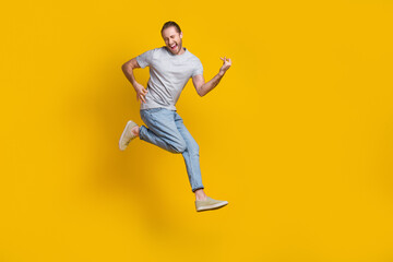 Obraz na płótnie Canvas Full length photo of cook cheerful man wear grey t-shirt jumping high playing guitar empty space isolated yellow color background