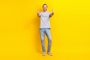 Full size photo of funny cheerful positive man gray t-shirt denim pants showing thumbs up nice work isolated on yellow color background