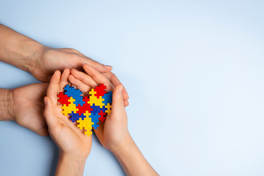 Woman and child hands holding together colorful puzzle heart on light blue background. World autism awareness day, Autism spectrum disorder concept