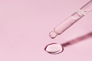 Macro drop of serum or oil with bubbles pouring from glass pipette on pink background. Cosmetic...