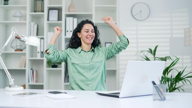 Happy joyful young hispanic woman office worker completed work on project dancing in the workplace Female Businesswoman, agent, employee or freelancer feels satisfied with laptop work well done Indoor
