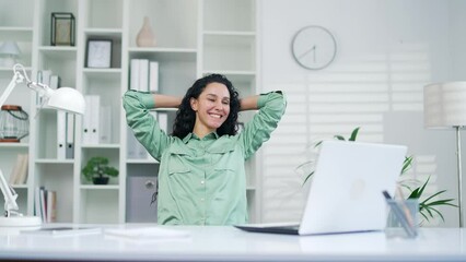 A satisfied glad young female worker employee relaxes after finishing work on a laptop computer Happy rejoices and rest leaning back in a chair job done at the workplace in office taking pause