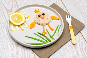 Easter funny creative healthy breakfast lunch food idea for kids, children. chicken shape sandwich from bread, peeled carrots, greens vegetables on plate wooden table background. Top view Flat lay