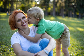 Little boy kisses his red haired young mother in park