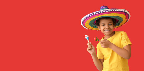 Funny Mexican boy in sombrero hat and with maracas on red background with space for text