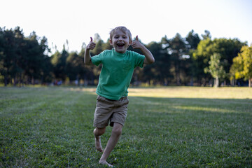 Close up portrait of smiling little boy in green T-shirt running in park