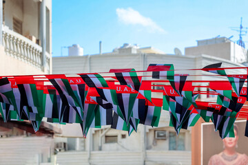 Hanging decorations from many national flags of United Arab Emirates on street of Dubai. Natoinal Day UAE. Flags in rows waving in wind against blue sky