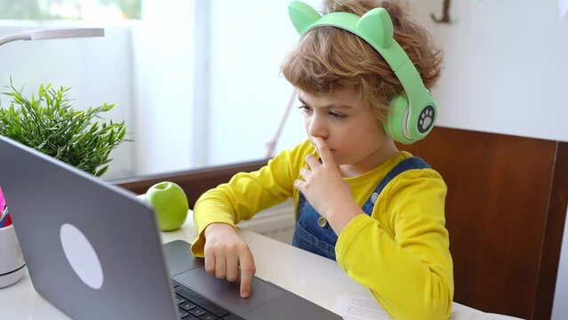Cute smart caucasian primary School Child with headphones playing video game hobby educate online laptop. Tutor teaching digital class, web lesson on computer at home. Virtual education course