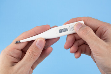 Men's hands hold a digital thermometer on blue background. a person looks at an electronic thermometer with temperature