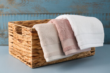 Wicker basket with soft towels on table near blue wooden wall
