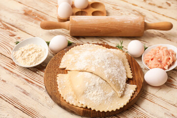 Board with raw empanadas, forcemeat, eggs, flour and rolling pin on light wooden background