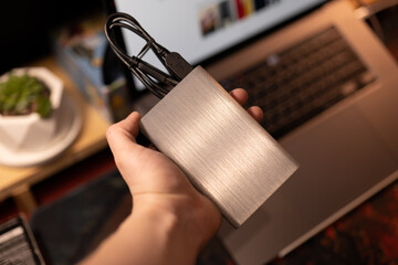 A man's hand holds a portable hard drive on the background of a laptop