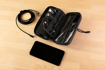 Opened cable organiser on a wooden table. Black bag, charger handbag, cables, power bank organizer for road trip, work vacation, business trip