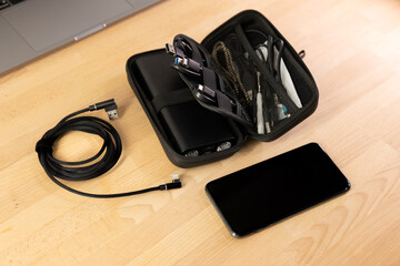 Cable and accessories organiser on a wooden table with a laptop. Black lightning cable, Black bag, charger handbag, smartphone cables, power bank organizer for road trip, work vacation, business trip