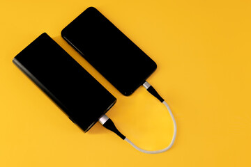 Mobile phone charges from black portable power bank with white cable on yellow background