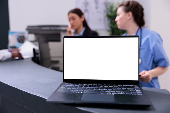 Laptop computer with white isolated screen standing on hospital registration counter during checkup visit appointment. Physician doctor discussing medical expertise with receptionist