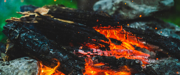 Obraz na płótnie Canvas Vivid smoldered firewoods burned in fire close-up. Atmospheric background with orange flame of campfire. Full frame image of bonfire. Warm whirlwind of glowing embers and ashes in air. Sparks in bokeh