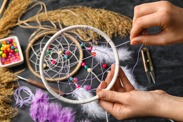 Woman making dream catcher on dark table, closeup