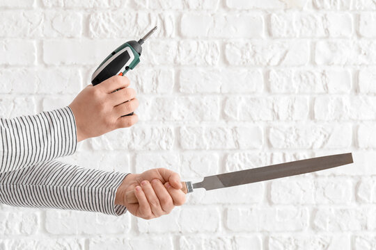Worker with screwdriver and file on white brick background