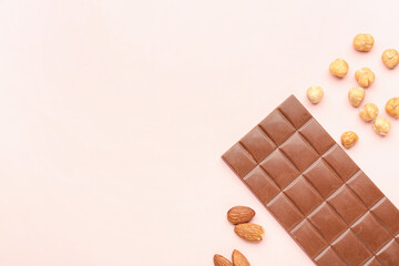 Tasty chocolate bar and nuts on color background