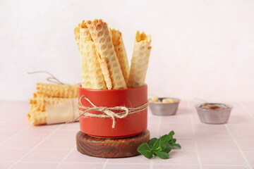 Wooden podium with bowl of delicious wafer rolls on pink tile table