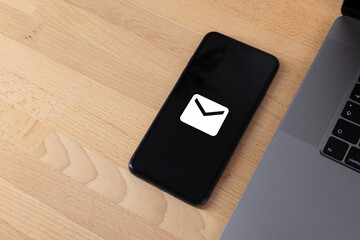 Unread email notification. New message on the smartphone screen. Mobile phone lies next to a laptop on a wooden table..