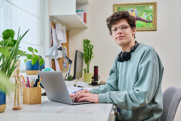 Young male college student sitting at desk at home using laptop