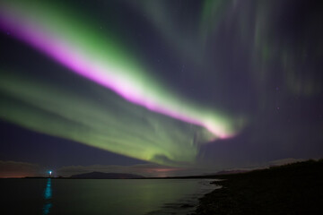 Naklejka premium Bright pink aurora borealis over ocen, Grotta lighthouse Iceland