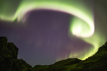 Bright aurora borealis spiral framing stars in mountain valley, Iceland